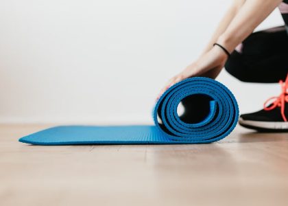 Side view of unrecognizable female athlete in black leggings and sneakers unfolding sport mat for fitness training indoors